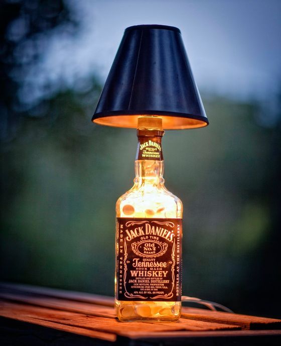Jack Daniel’s whiskey bottle repurposed as a table lamp with a black lampshade, glowing warmly on a wooden surface