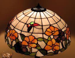 Stained-glass table lamp with orange flowers and green leaves, lit warmly against a dark background