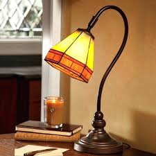 Amber-tinted desk lamp on a wooden table beside a lit candle and books by a window