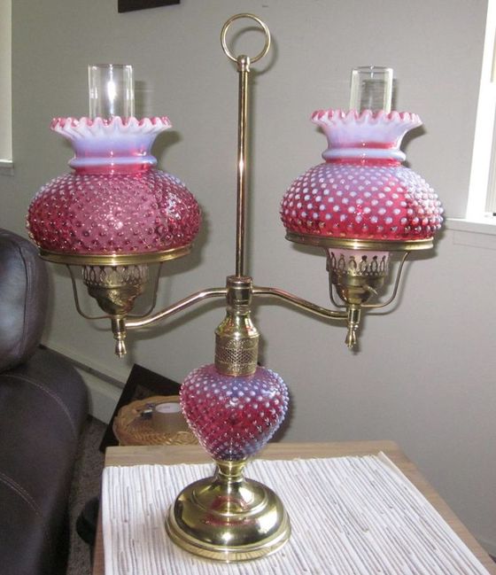 Pink glass table lamp with two ornate shades and brass base on a table