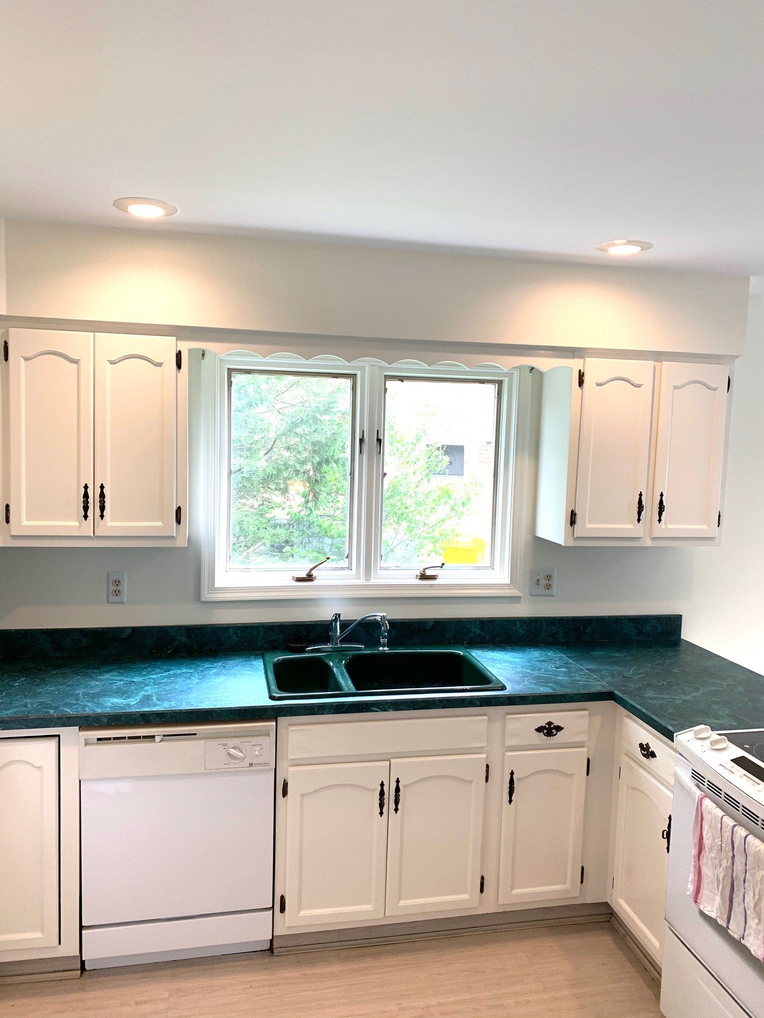 White kitchen with green countertops, double sink under a window, and white cabinets and appliances.