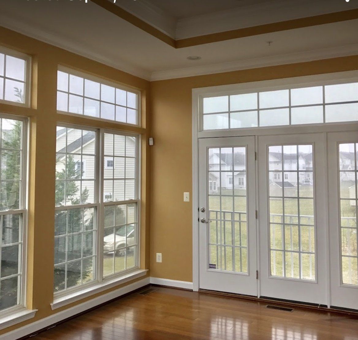 Empty sunroom with large windows, glass double doors, tan walls, and hardwood floors.