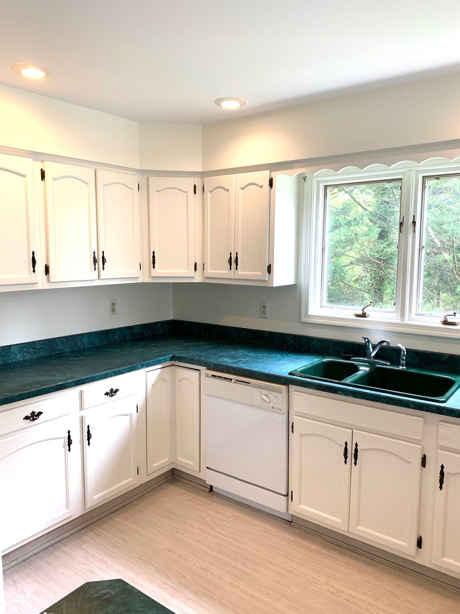 Bright white kitchen with dark countertops, white cabinets, and a window overlooking greenery.
