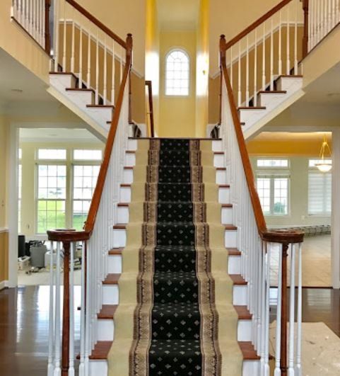 Grand foyer with a central carpeted staircase, white railings, and large windows filling the bright interior with light