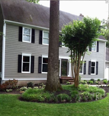 Gray two-story house with black shutters and landscaped front yard with trees and shrubs