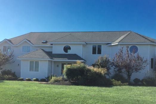 Suburban two-story white house with gray roof and front lawn under a clear blue sky