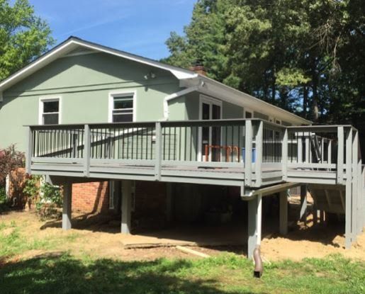 Raised green house with a large wooden deck and stairs in a sunny yard