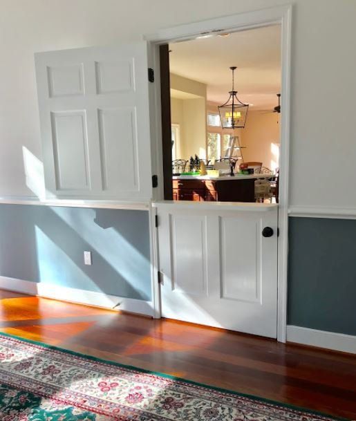Open white double doors reveal a warmly lit kitchen from a hardwood-floored dining room.