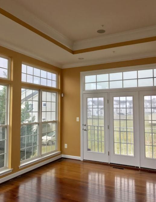 Bright empty room with hardwood floors, large windows, and glass double doors overlooking a field