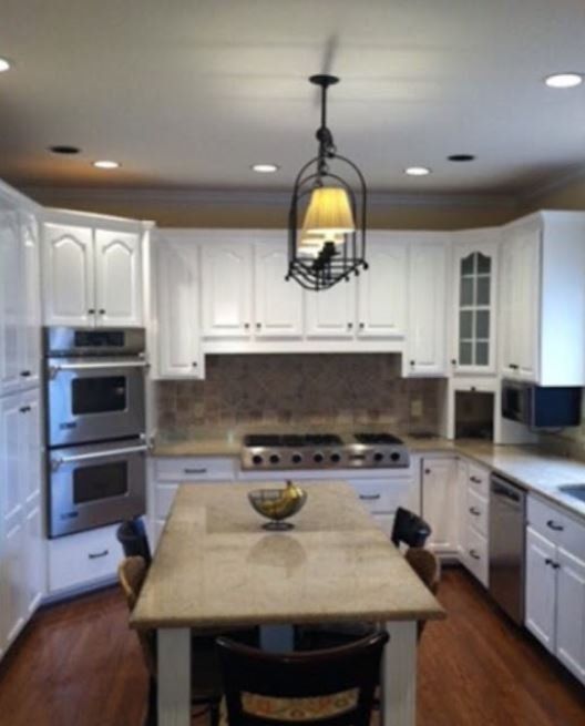 Bright white kitchen with island, stainless appliances, and hanging pendant light.