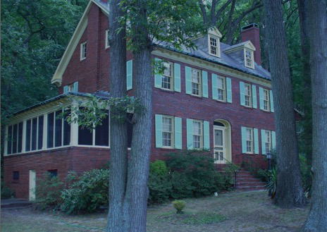 Red brick colonial house with white trim, dormer windows, and a screened porch amid trees