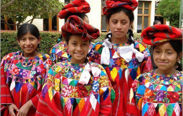 Mädchen in farbenfroher, bestickter traditioneller guatemaltekischer Kleidung, lächelnd.