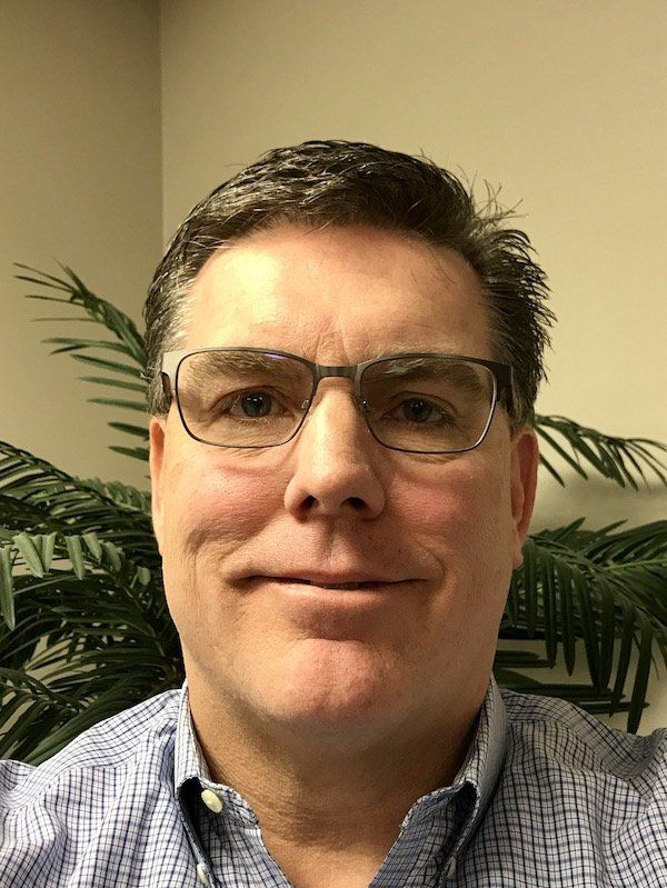 A man wearing glasses and a plaid shirt is smiling for the camera.