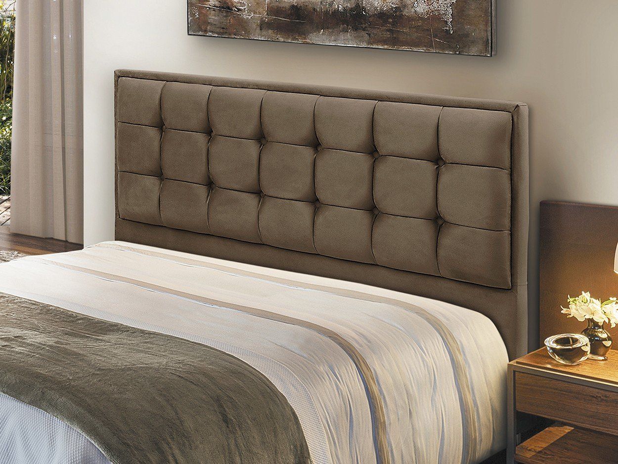 Cabeceira estofada marrom sobre uma cama com manta estampada e mesa de cabeceira.