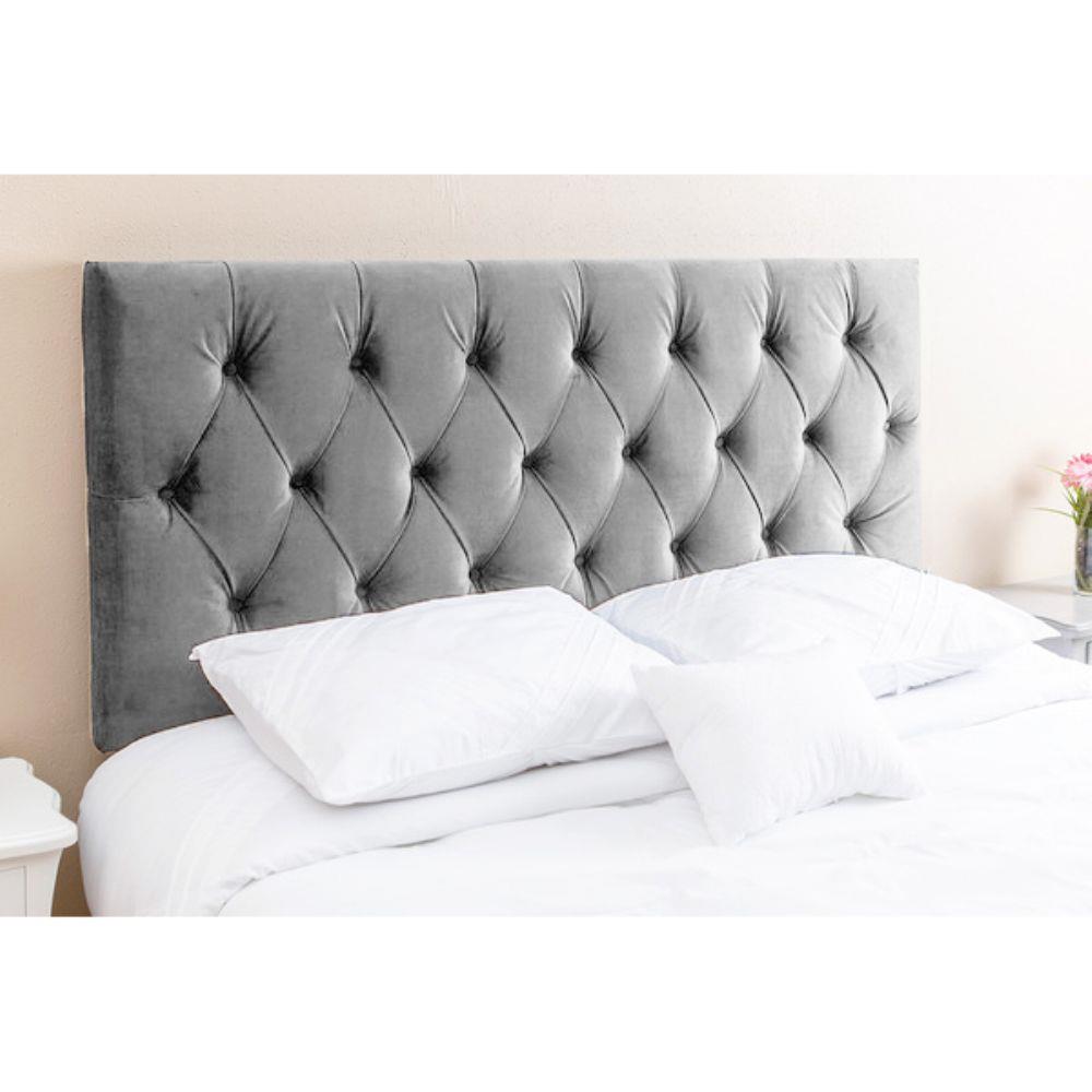 Cabeceira de veludo cinza com capitonê acima de uma cama com roupa de cama e travesseiros brancos.