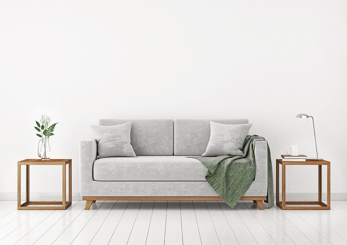 Uma sala de estar moderna com um sofá cinza, duas mesas laterais de madeira e uma manta verde.