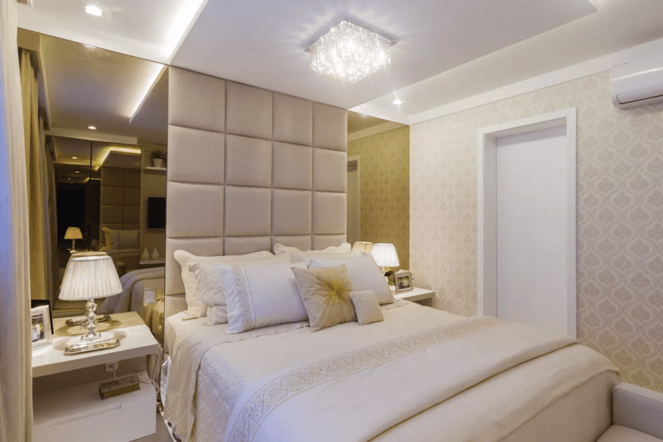 Quarto elegante com paredes espelhadas, cabeceira estofada, cama, mesas de cabeceira e lustre.