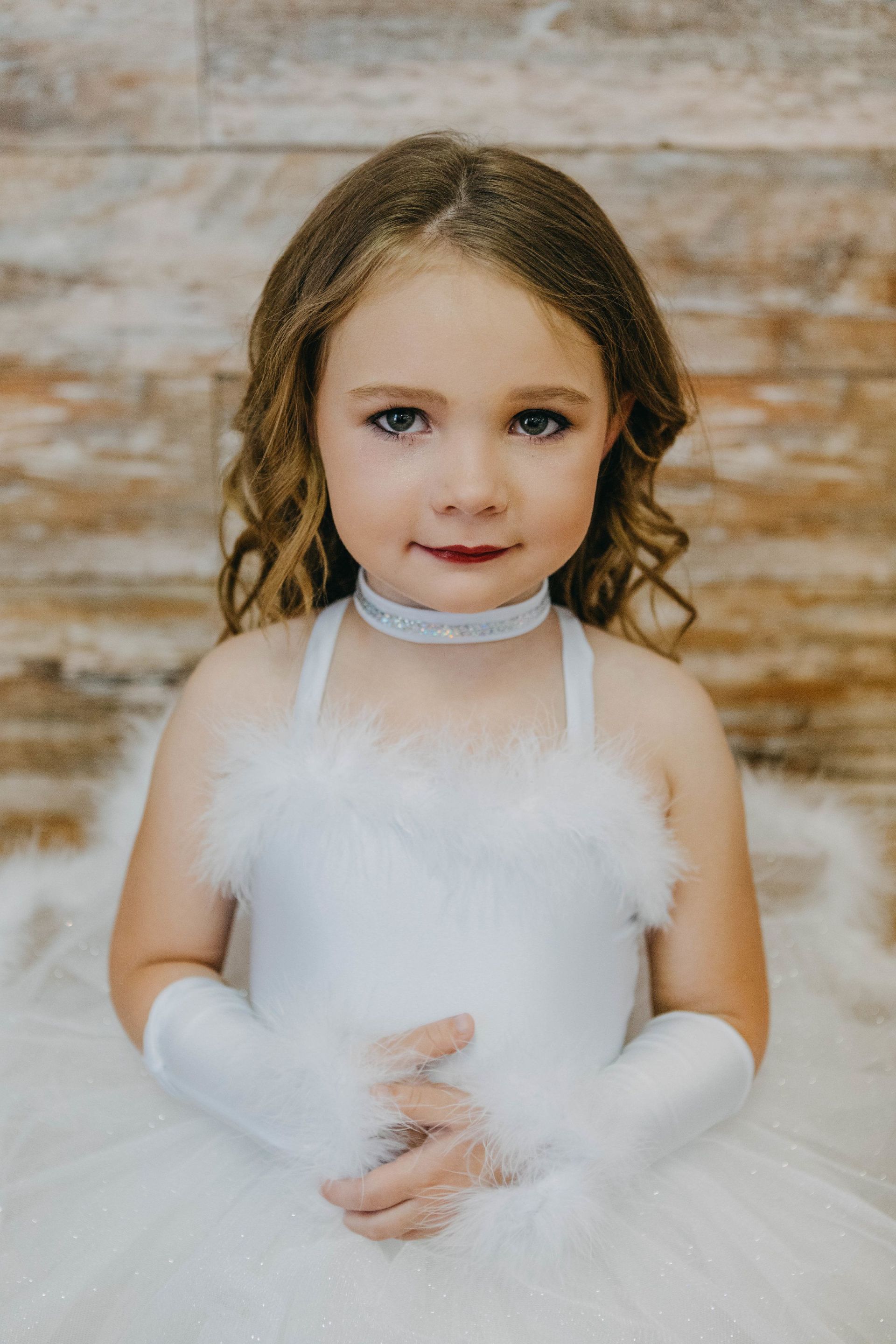 A little girl is wearing a white dress and white gloves.