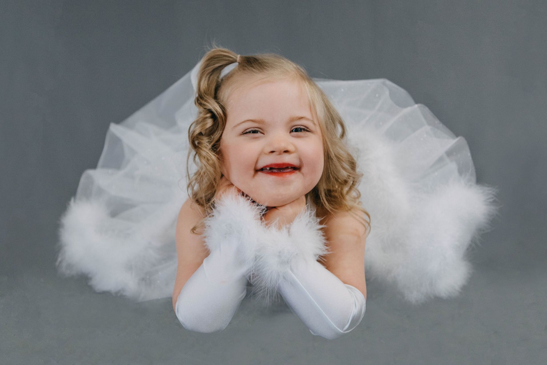 A little girl dressed as an angel with white wings and gloves.