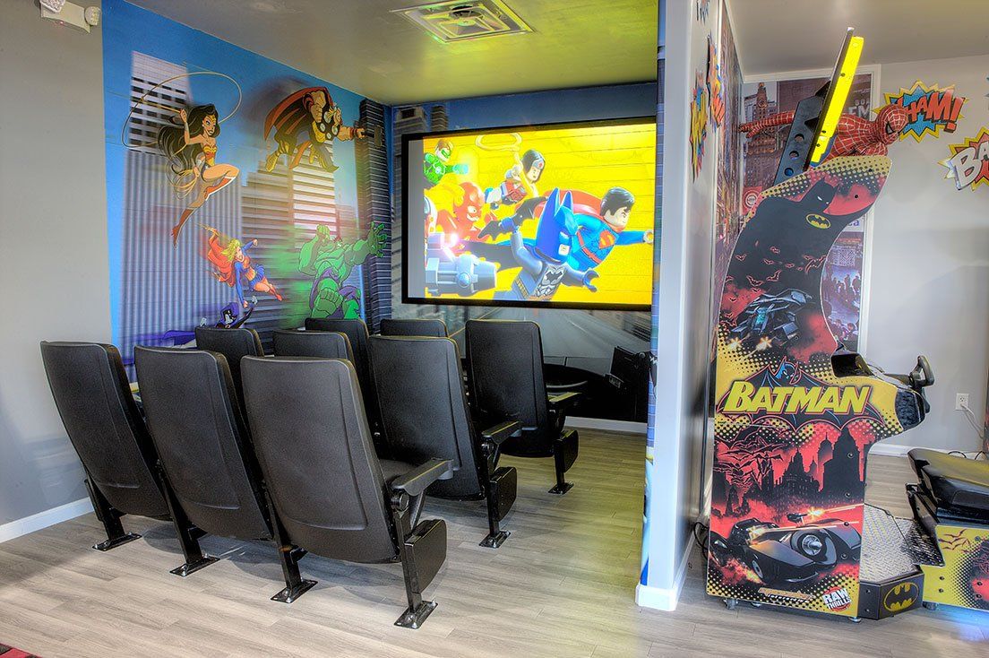 A movie theater with a projector screen and a batman arcade machine.