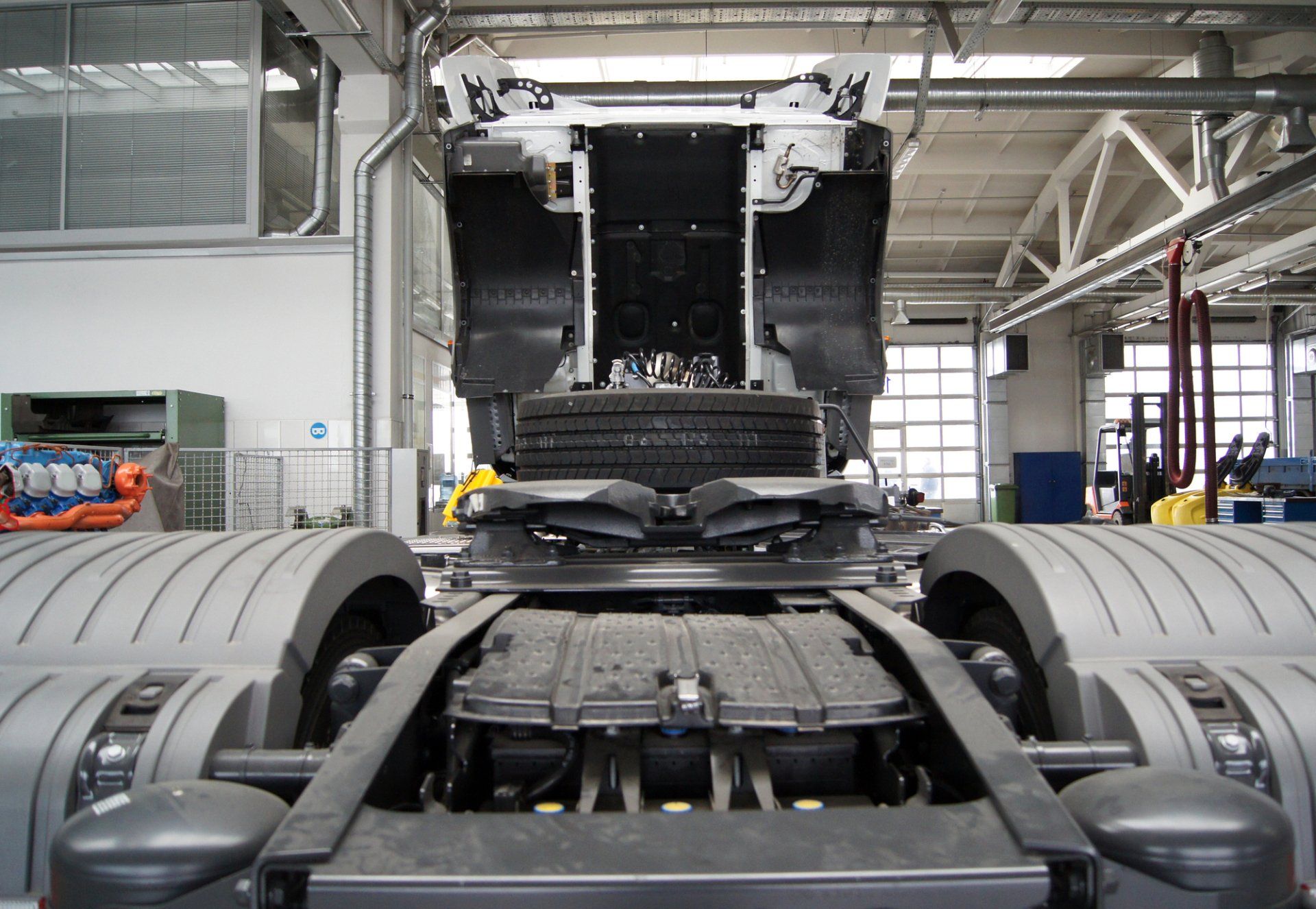 A semi-truck chassis and fifth wheel assembly inside a brightly lit manufacturing facility.