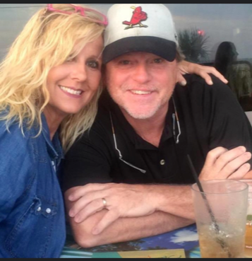 A smiling couple poses for a photo, sitting at a table with a drink.