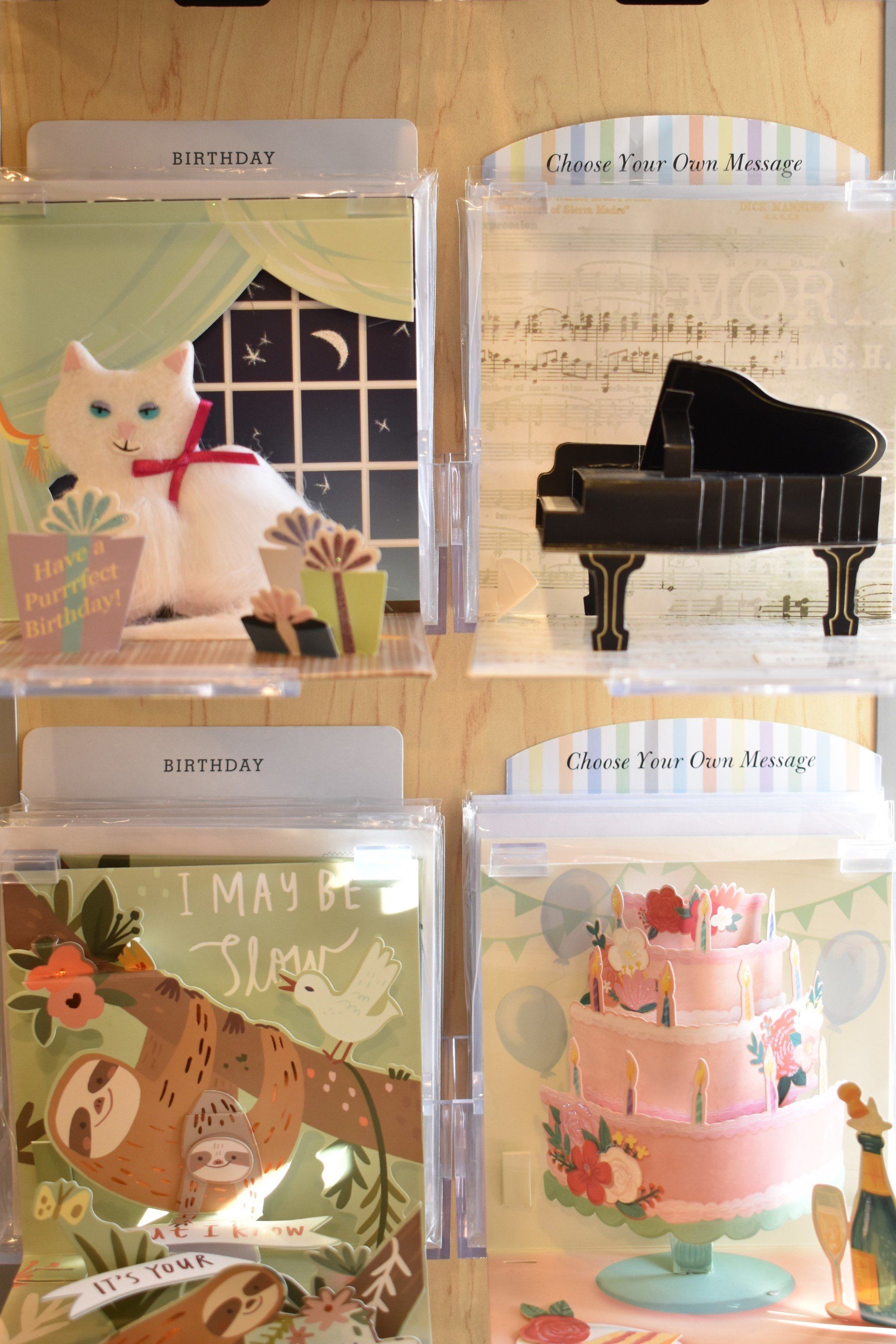 A display of greeting cards with a cat , a piano and a cake