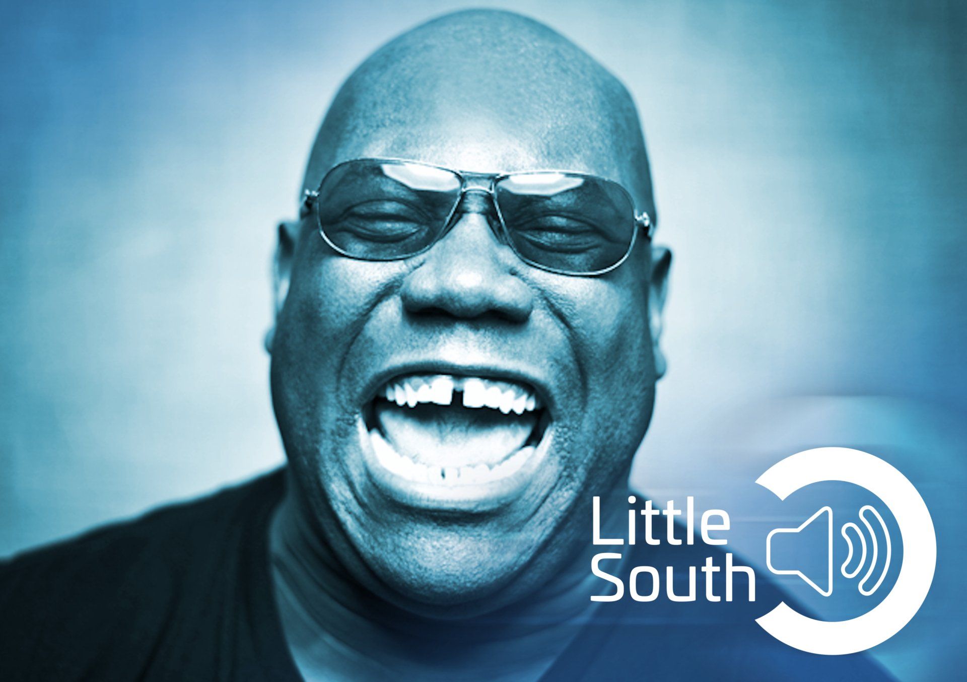 A man wearing sunglasses is laughing in front of a little south logo