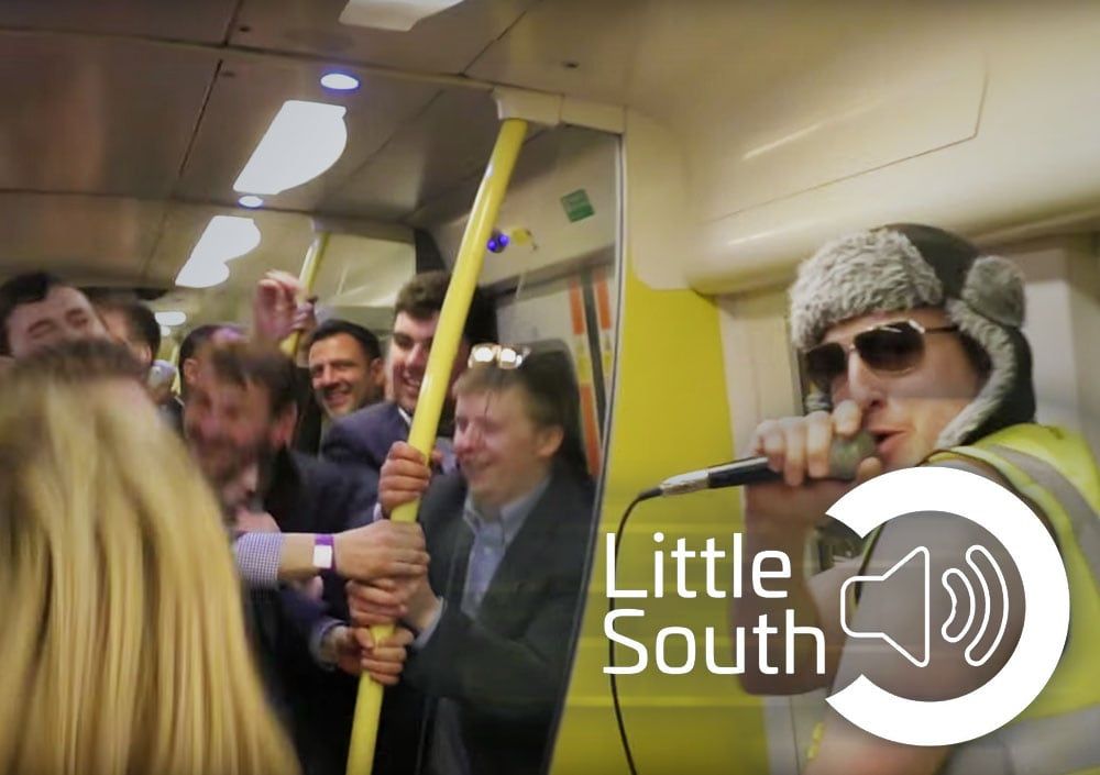 A man singing into a microphone on a train with the words little south on the bottom