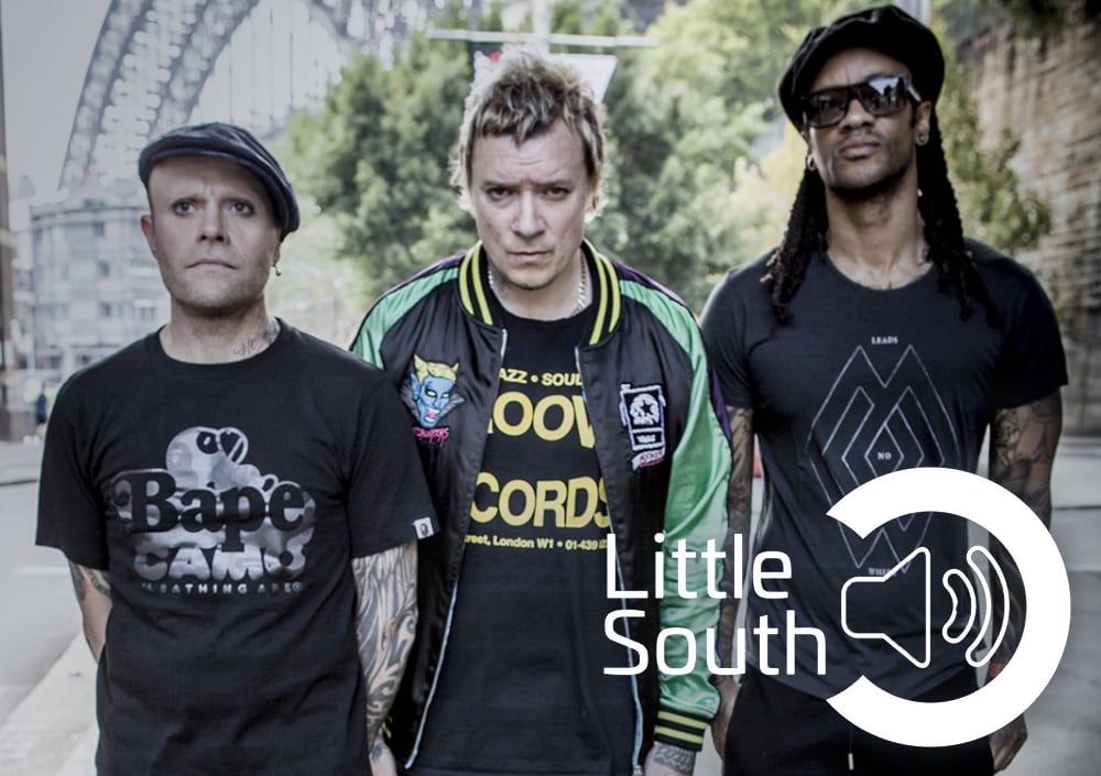 Three men are standing next to each other in front of a sign that says little south