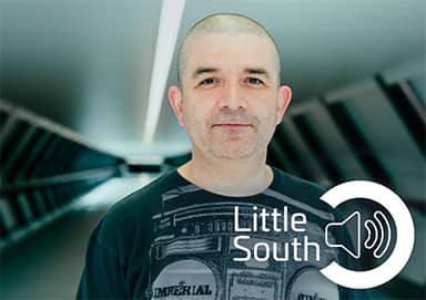 A man wearing a little south shirt is standing in a room.