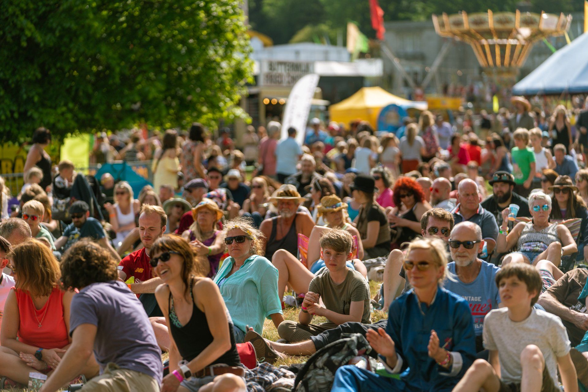 A large group of people are sitting in the grass at a festival.