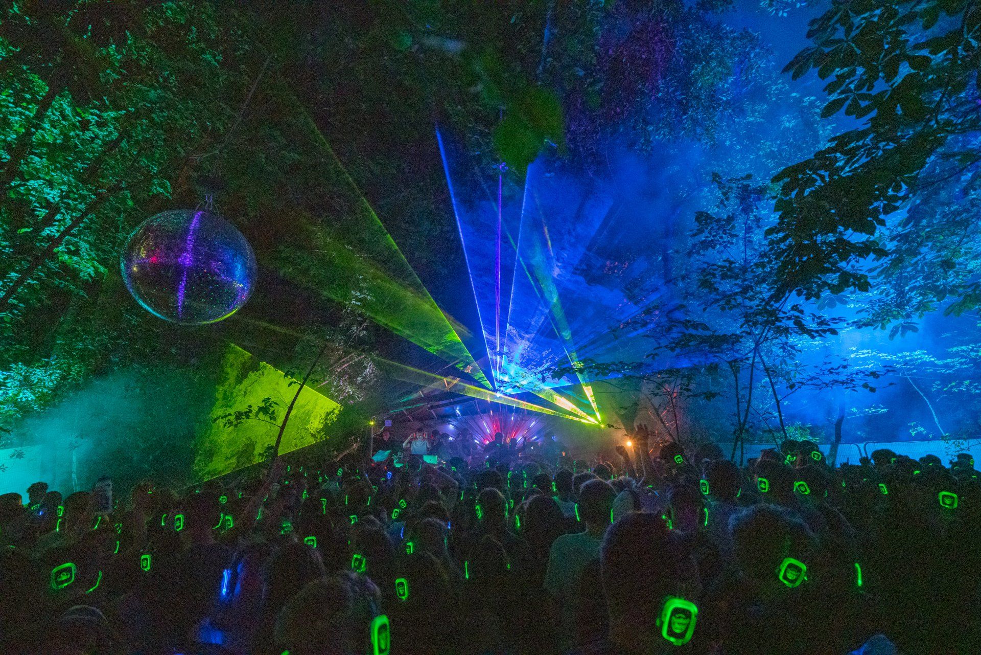 A crowd of people are standing in front of a stage with a lot of lights coming out of it.