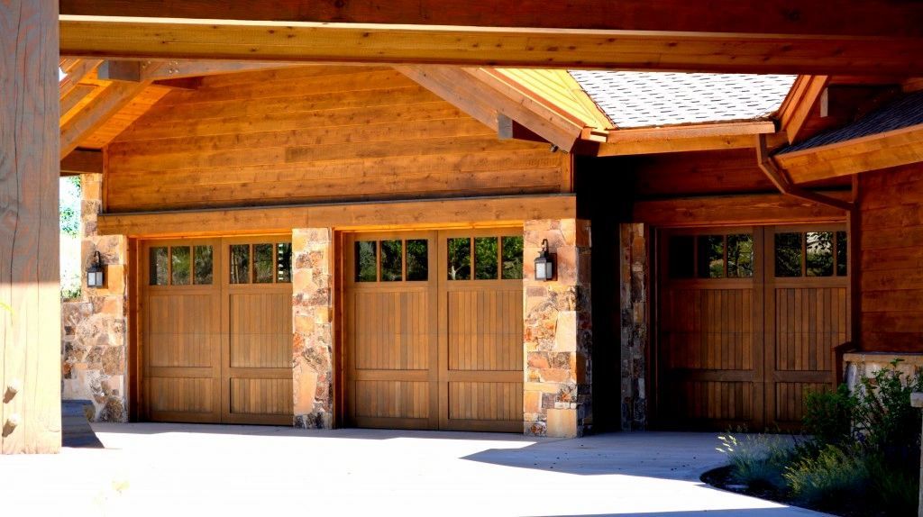Three wooden garage doors with stone accents and a wood beam overhang.
