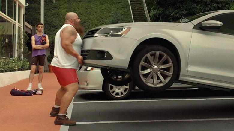 Um homem barbudo está levantando um carro em um estacionamento.