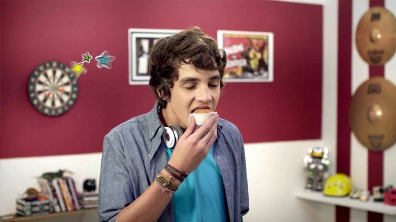 Um jovem está comendo um donut em uma sala com um alvo de dardos.