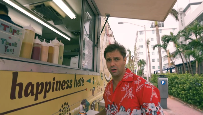 Um homem de camisa vermelha está parado na frente de um food truck que diz felicidade aqui.