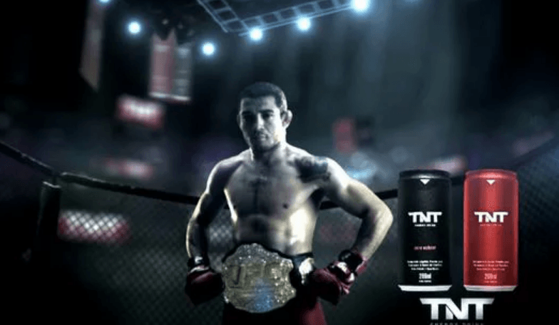 Um homem em um ringue de boxe ao lado de duas latas de tnt