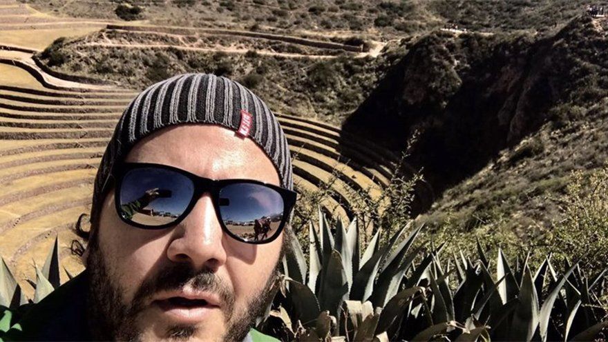Um homem usando óculos escuros e um gorro está parado em frente a uma montanha.