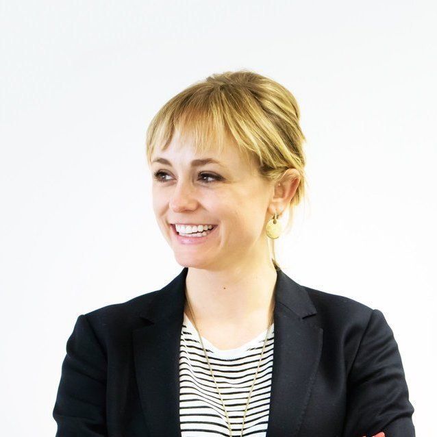 A woman wearing a black jacket and striped shirt is smiling