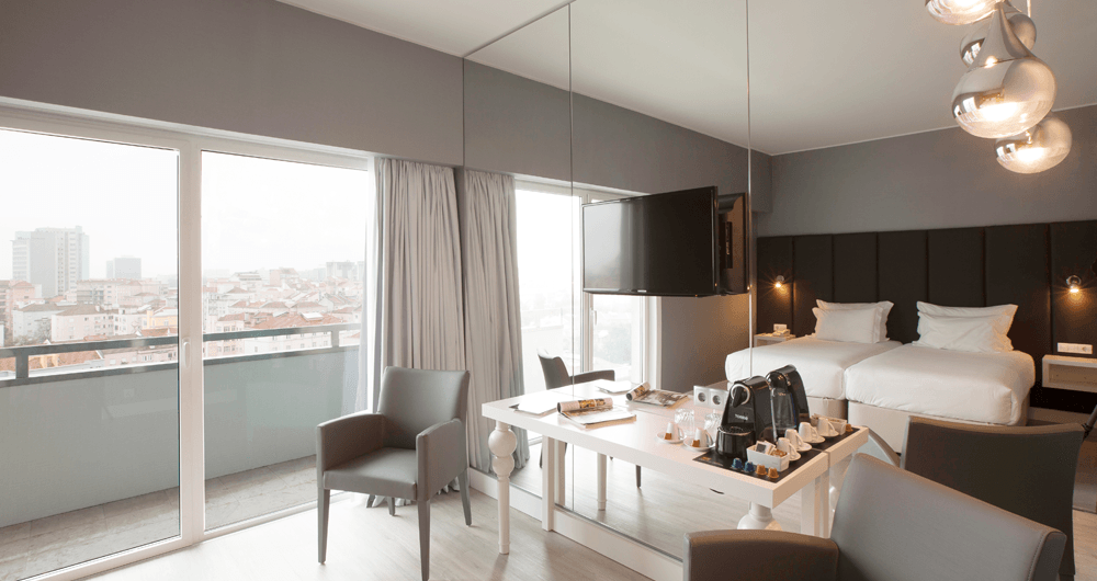 Um quarto de hotel com duas camas, uma mesa, cadeiras e uma varanda.