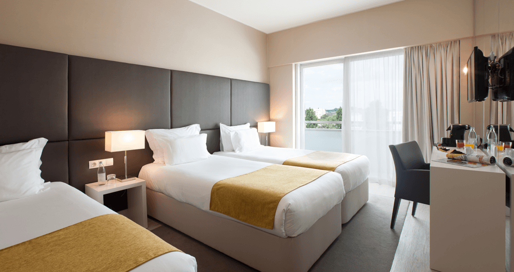 Um quarto de hotel com duas camas, uma escrivaninha e uma televisão.