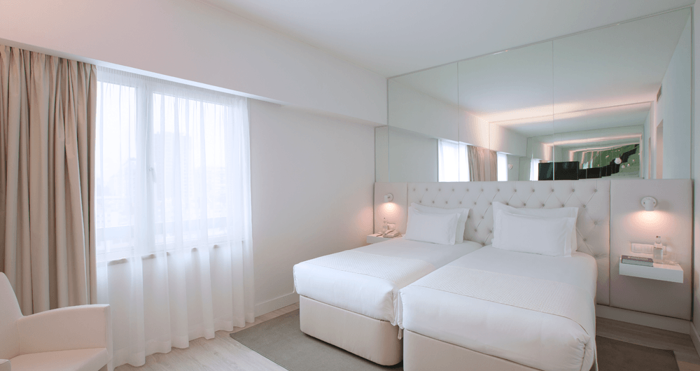 Um quarto de hotel com duas camas, uma cadeira e um espelho grande.