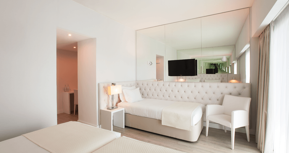 Um quarto de hotel com uma cama, cadeira, televisão e espelhos.
