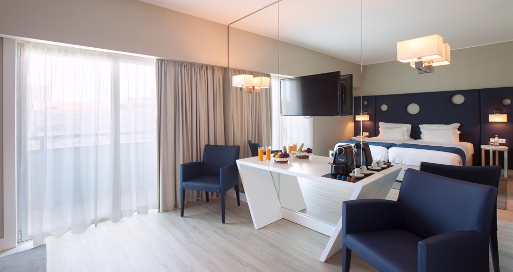 Um quarto de hotel com duas camas, uma mesa, cadeiras e uma televisão.