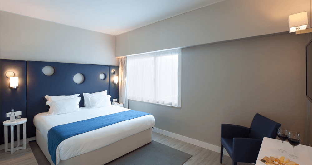 Um quarto de hotel com uma cama, cadeira, mesa e televisão.