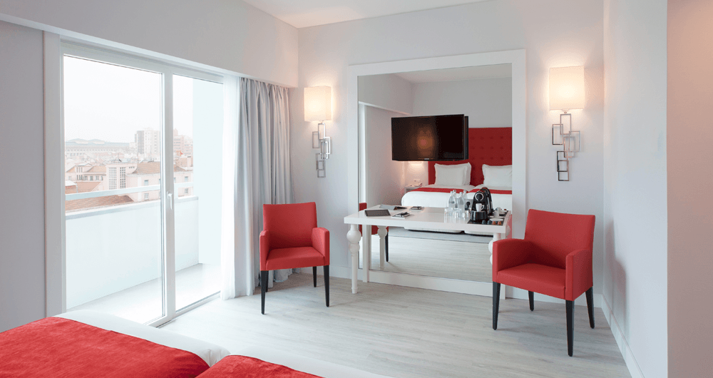 Um quarto de hotel com uma cama, escrivaninha, cadeiras e um espelho grande.