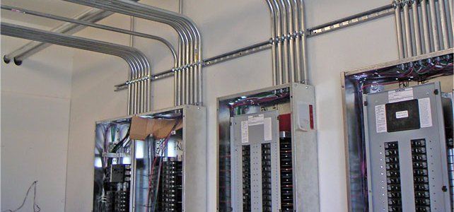 Electrical conduits and panels installed on a white wall in an unfinished space.