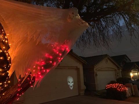 Halloween yard display with glowing orange spider web, red lights, skull projection, and lit pumpkins at dusk