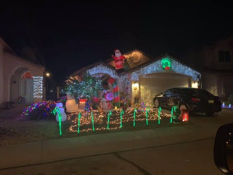 House lit with colorful Christmas lights and decorations at night, with a car parked in front.